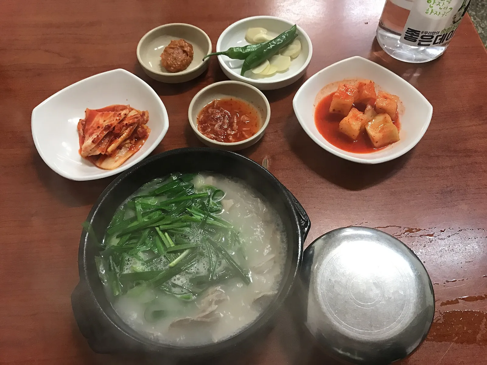 A stone pot of dwaeji gukbap, pork and rice soup topped with chives, with kimchi, radish kimchi and other side dishes