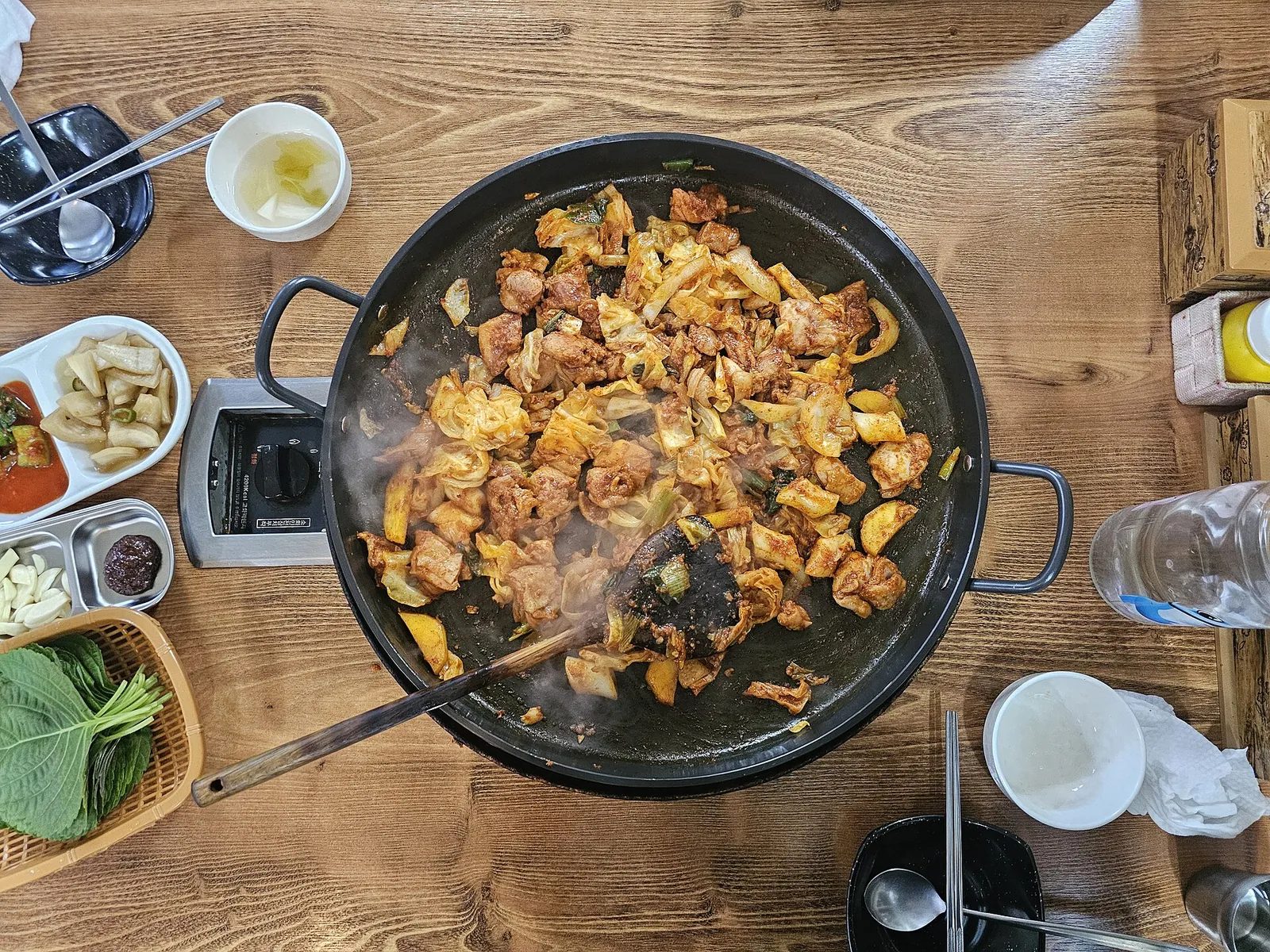 Dakgalbi, spicy chicken with cabbage, cooking on a round iron griddle over a tabletop burner, with perilla leaves on the side