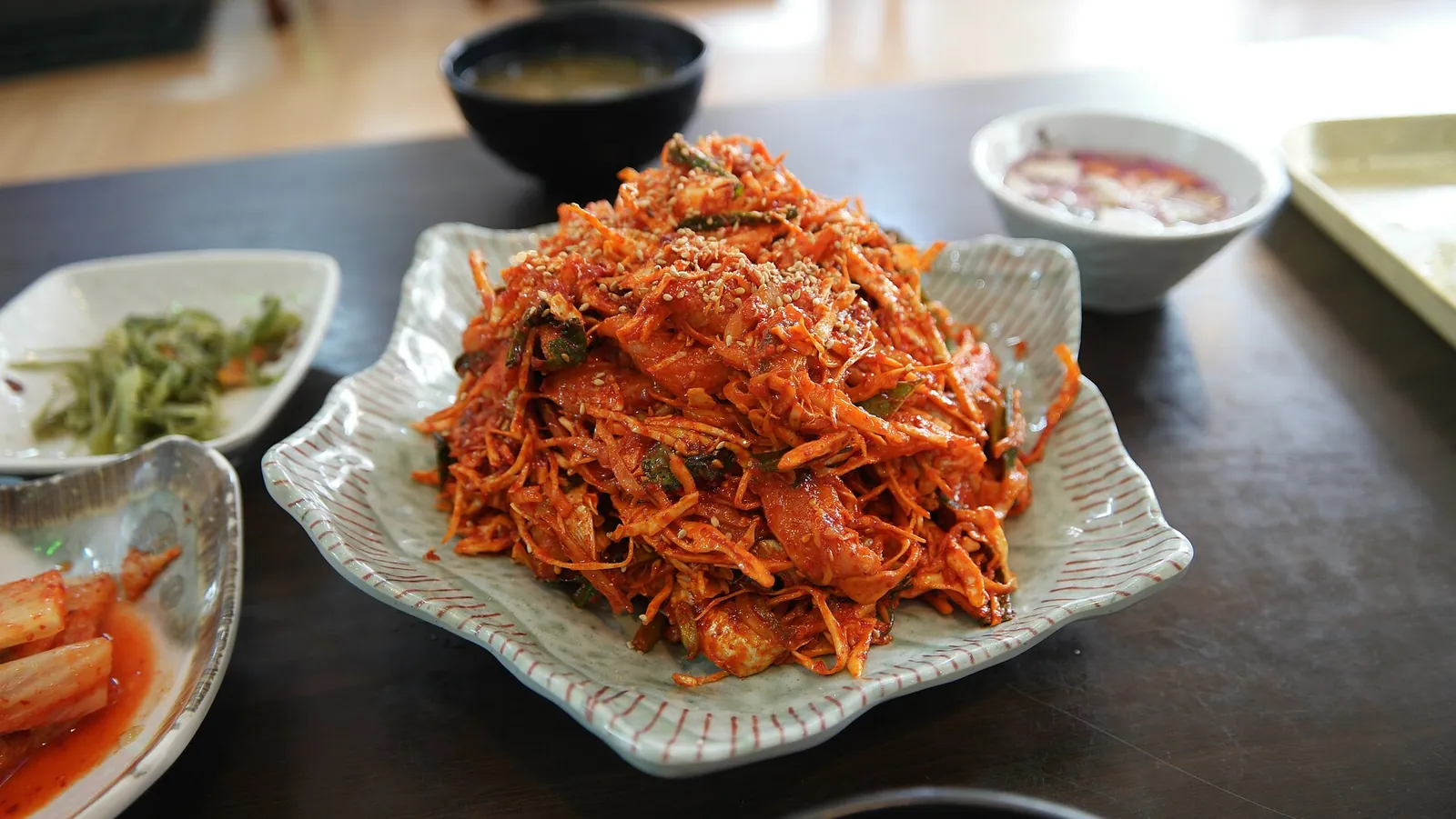 A plate of baendaengi hoe muchim, sliced raw scaled sardine mixed with vegetables in red chilli sauce, with side dishes