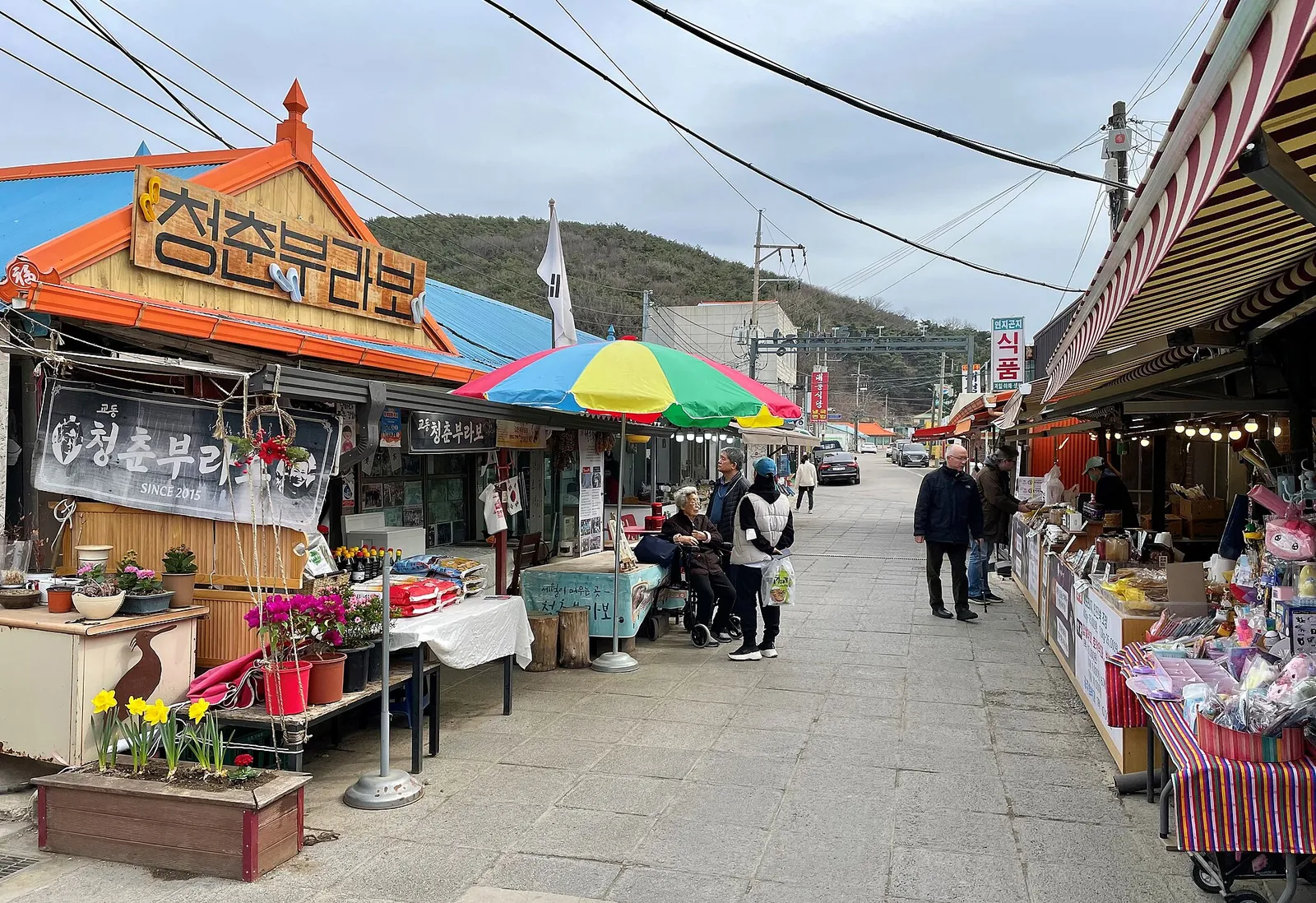 Market alley in Daeryong-ri on Gyodongdo with shop signs, umbrellas and stalls along a paved lane