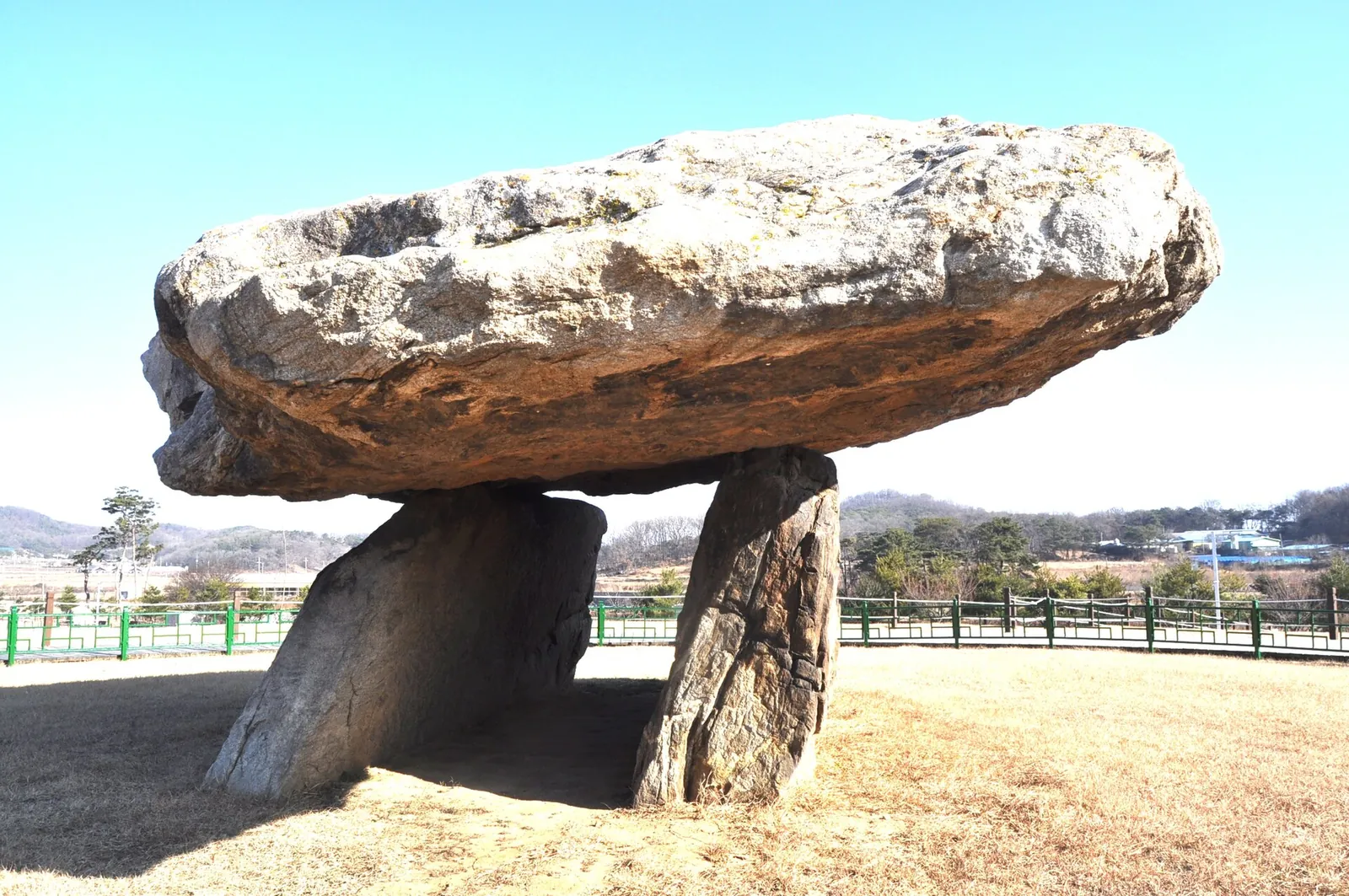 A large flat capstone resting on two upright stones in an open field under a blue sky