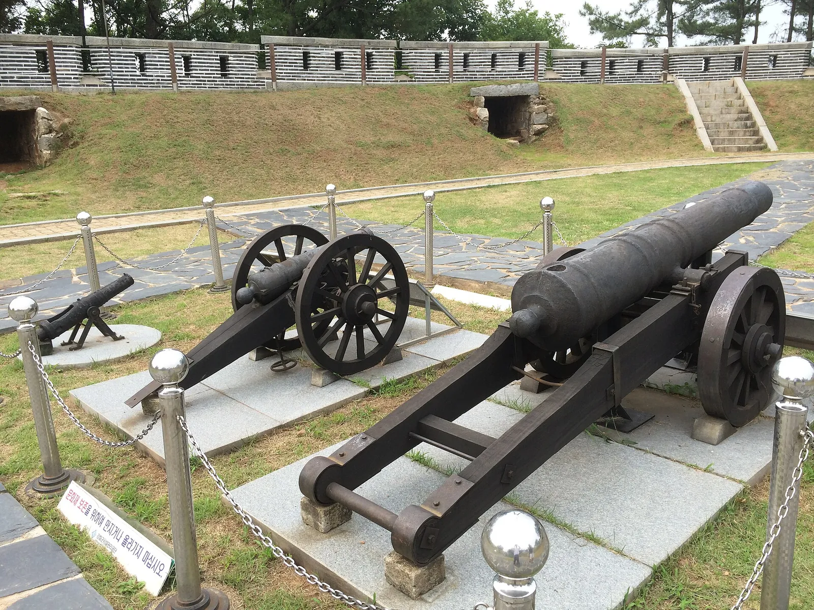 Two old cannons on wooden-wheeled carriages displayed on a stone platform inside the walls of Gwangseongbo