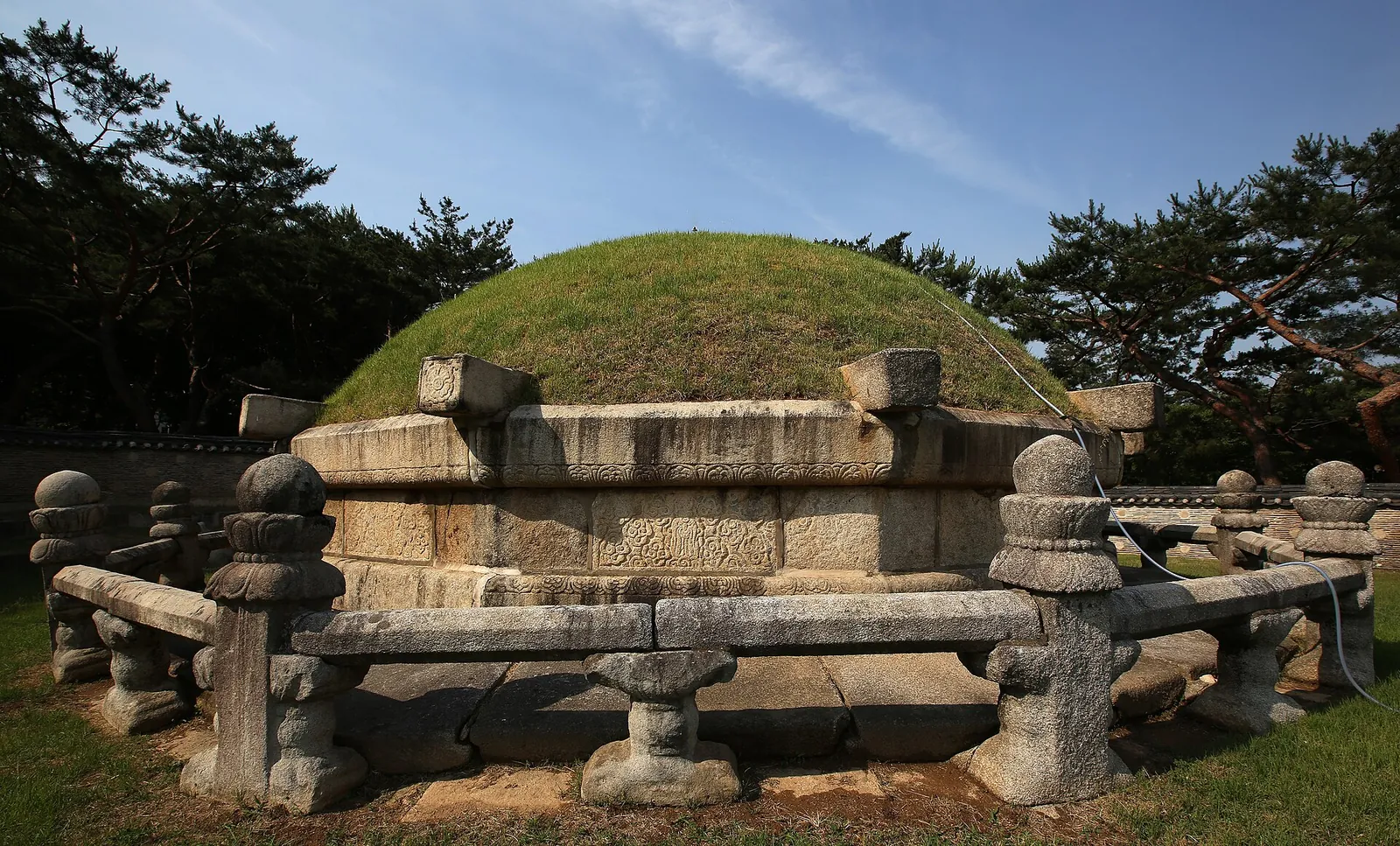 Grass burial mound ringed by carved stone screens and railings at Seolleung royal tomb