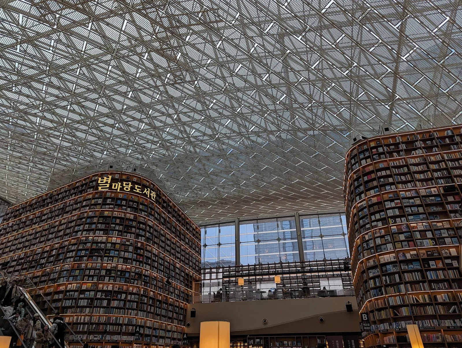 Curved floor-to-ceiling bookshelves under the glass roof of Starfield Library in COEX Mall