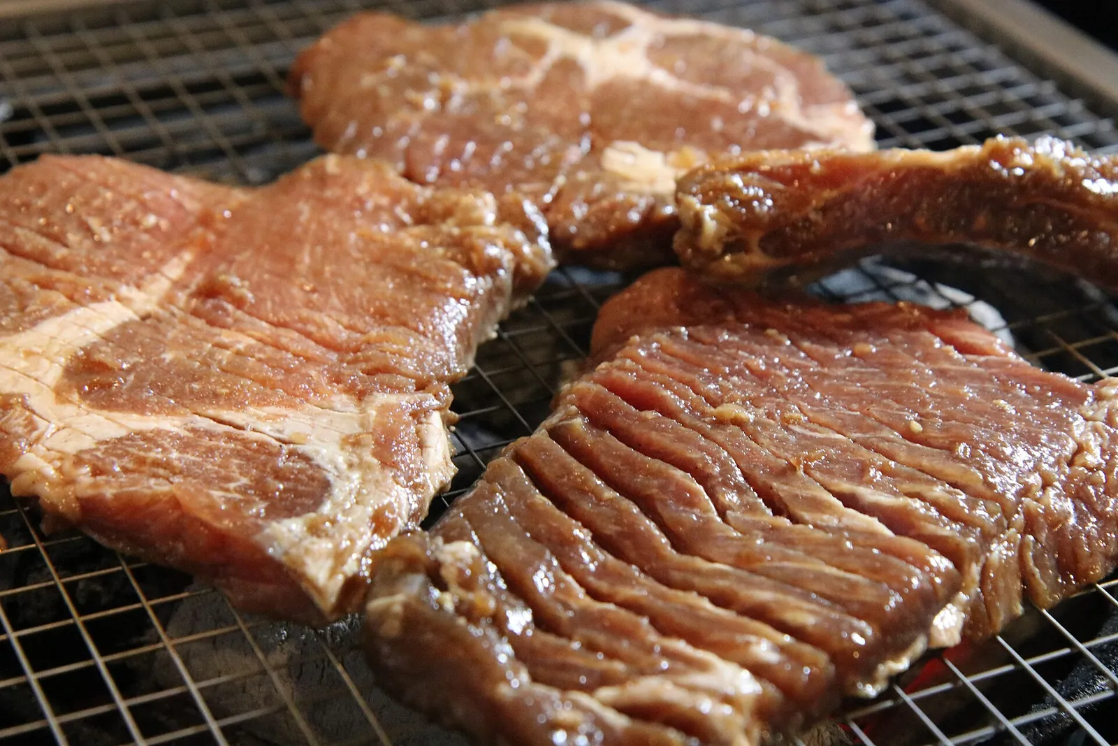 Marinated beef galbi ribs grilling on a wire grill over charcoal