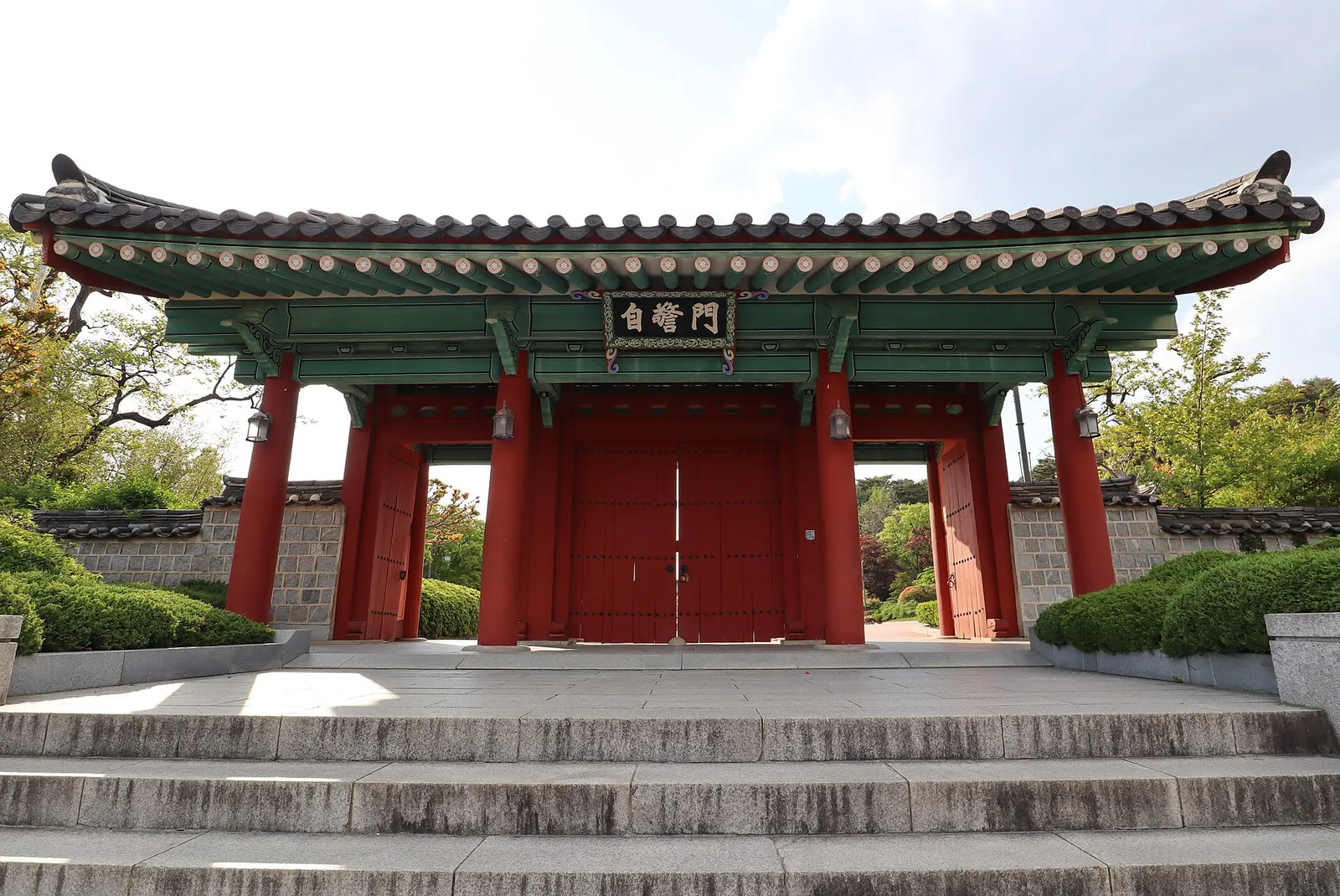Red-pillared gate with a painted tiled roof at the top of stone steps in the Ojukheon grounds