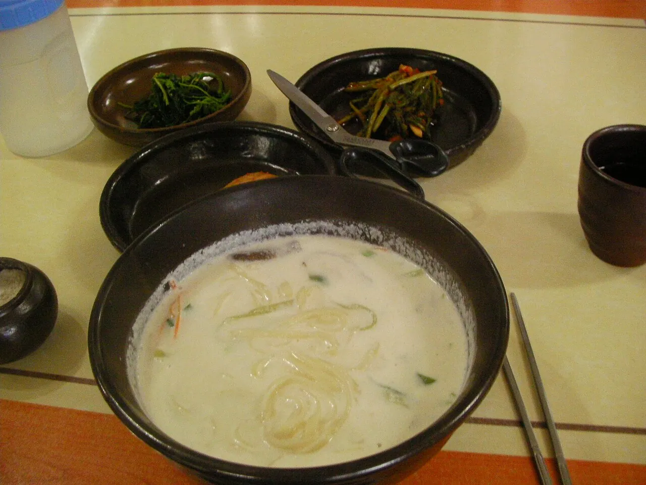 A bowl of pale jatguksu noodles in cold pine-nut soup with small side dishes