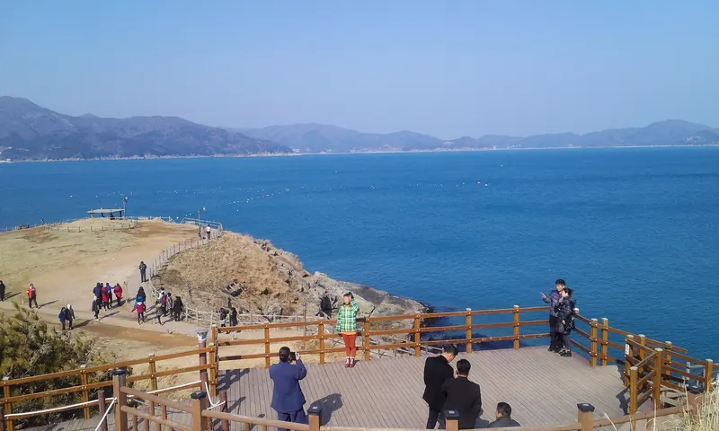 Visitors on the wooden viewing deck at Windy Hill in Geoje, looking out over a deep-blue sea and distant islands