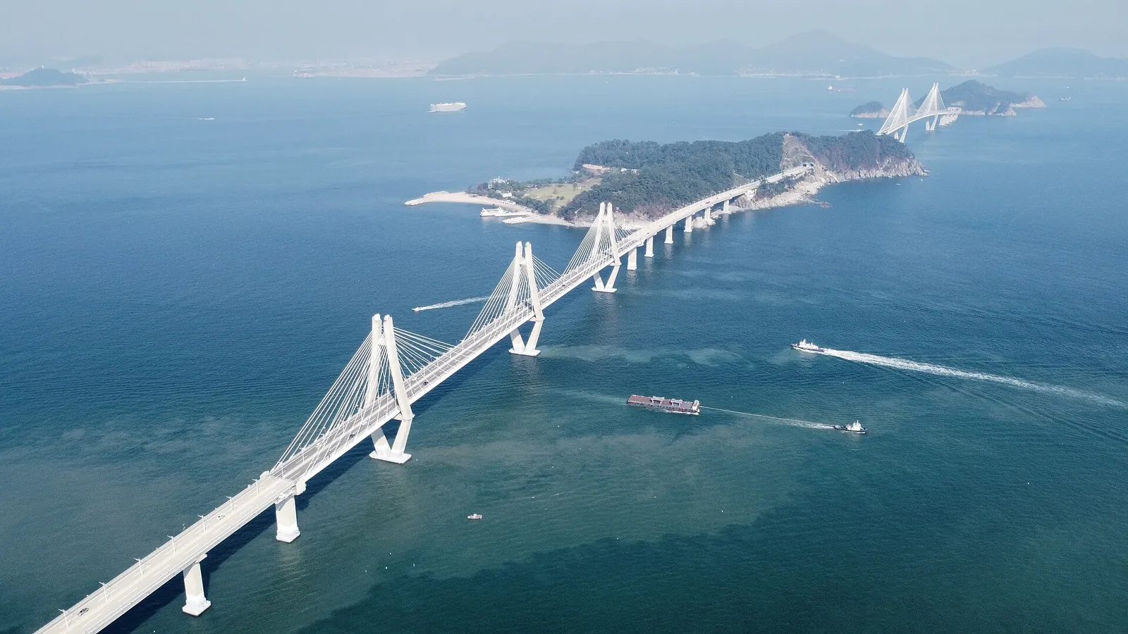 The cable-stayed towers of the Busan–Geoje road link crossing open sea between wooded islands