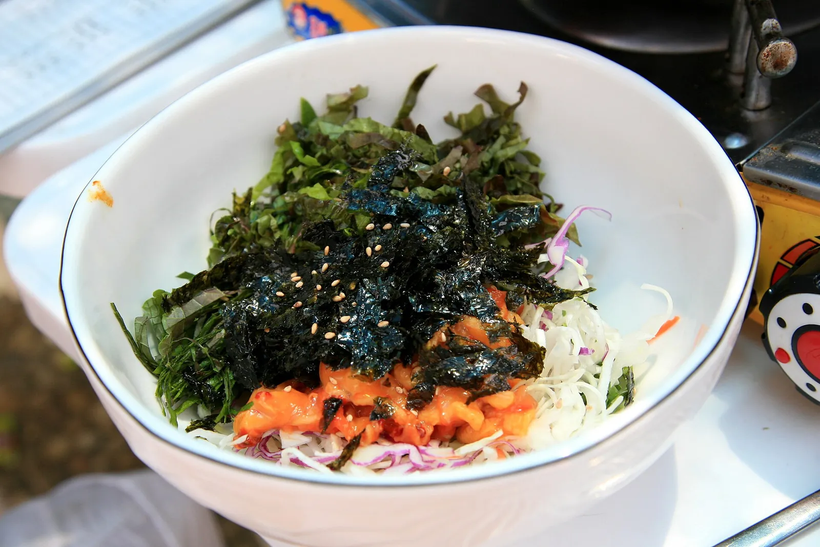 A bowl of meongge bibimbap: rice topped with chopped sea squirt, shredded laver, lettuce and sesame