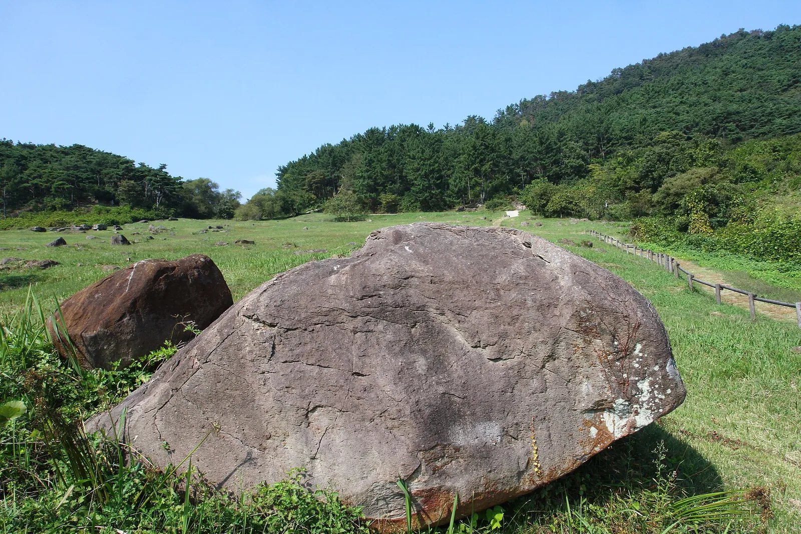 Large dolmen capstones scattered across a grassy hillside under a blue sky in Jungnim-ri, Gochang