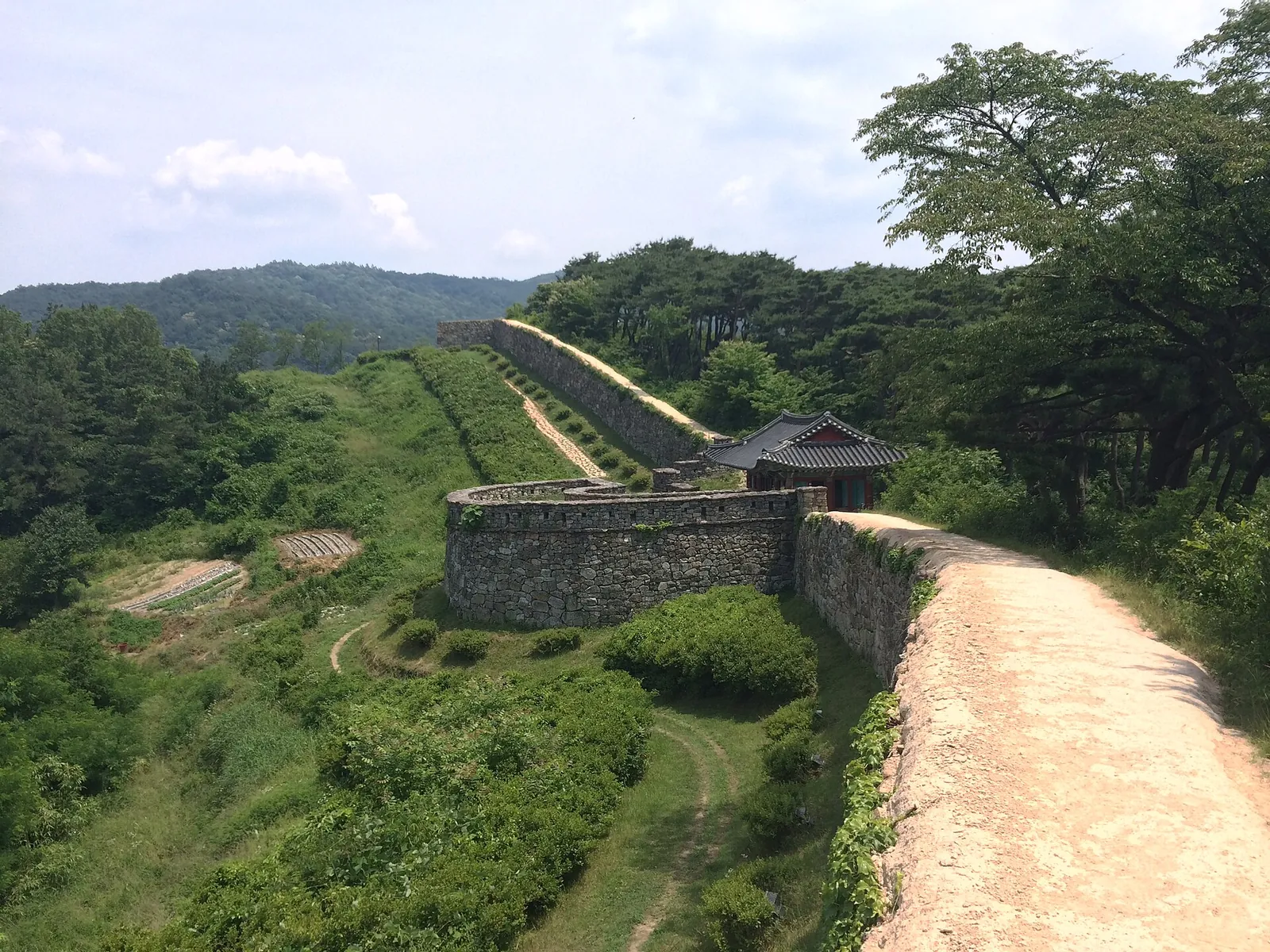 Stone wall of Gochangeupseong curving over a green hillside with a gate pavilion below
