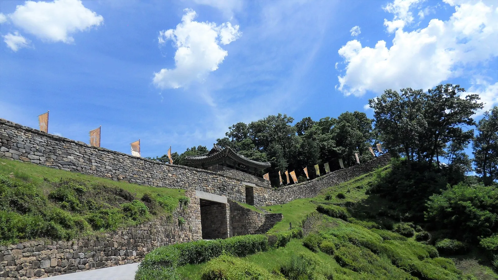 Stone walls of Gongsanseong Fortress climbing a green slope to the Geumseoru gate pavilion under a blue sky