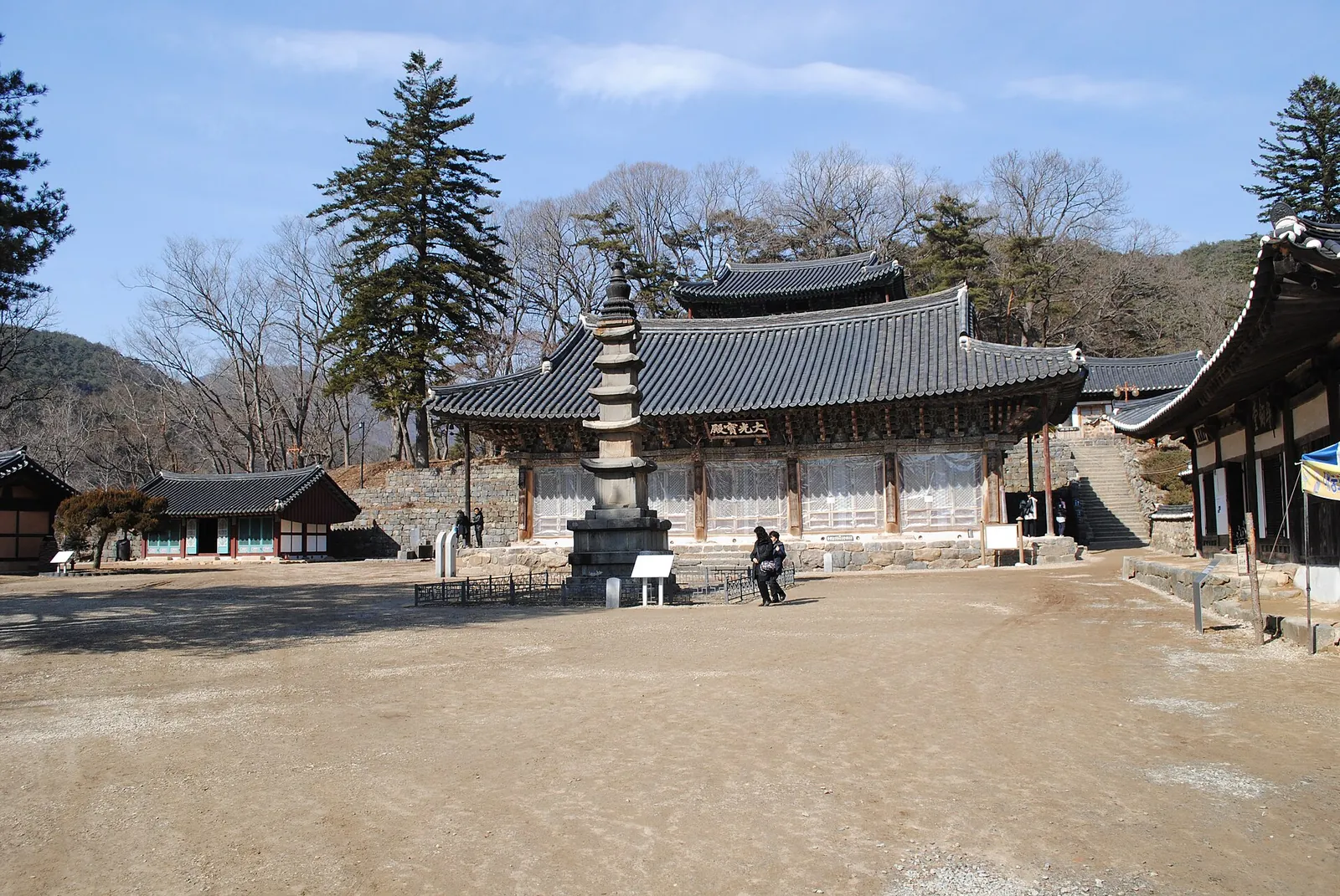 Courtyard of Magoksa temple with a stone pagoda in front of a tiled-roof hall and pine-covered hills