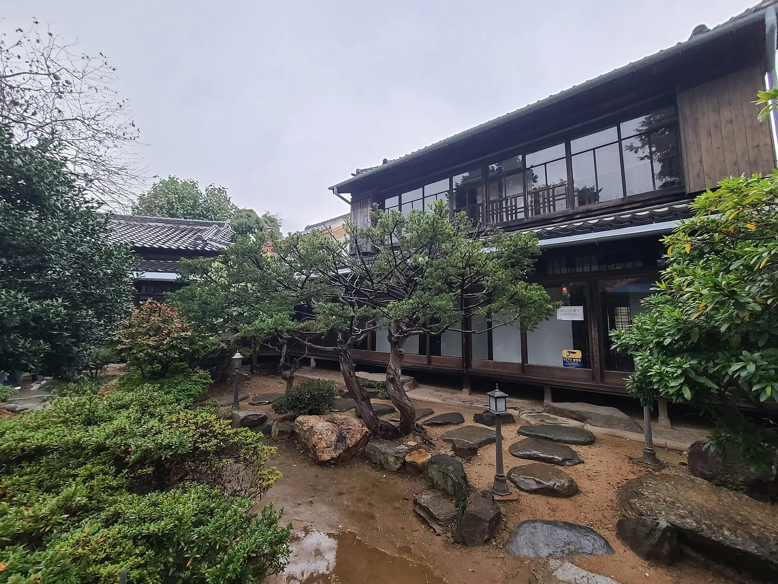 Two-storey Japanese-style timber house behind a garden of rocks, pines and stone lanterns