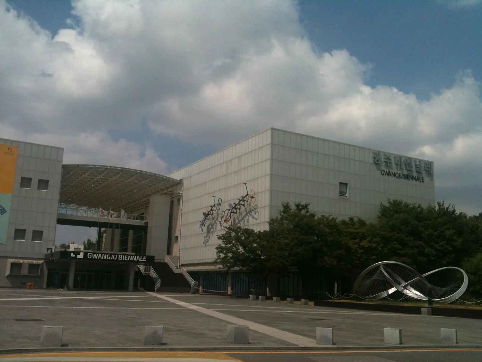 The modern exhibition building of the Gwangju Biennale with its glass entrance and a curved metal sculpture on the forecourt