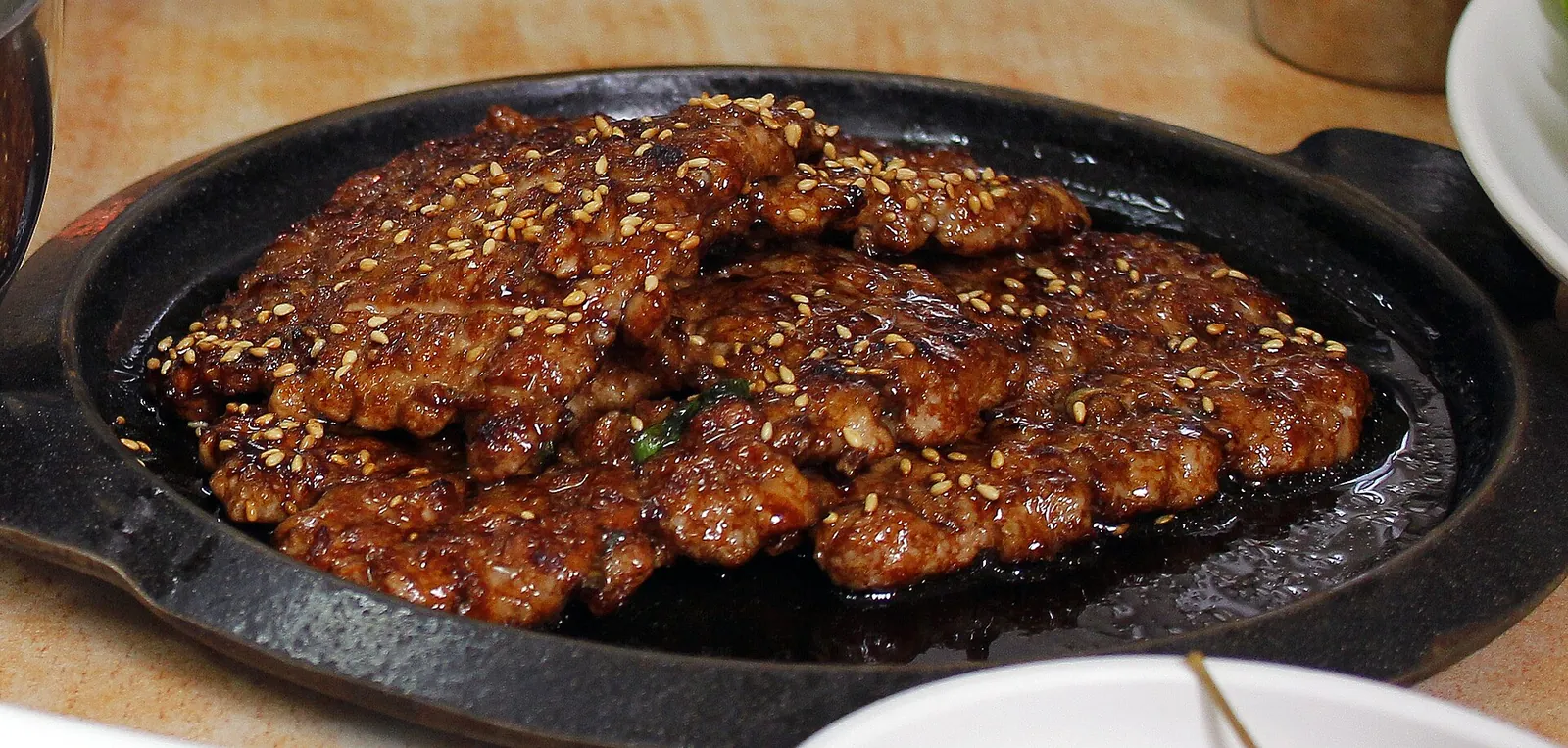 Glazed tteokgalbi patties sprinkled with sesame seeds on a black cast-iron plate