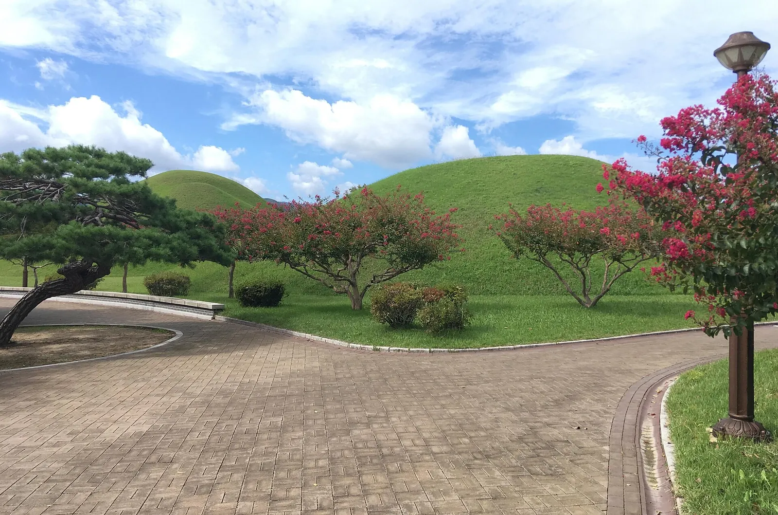 Grass-covered Silla royal tombs and a paved path in Daereungwon, Gyeongju, under a blue sky