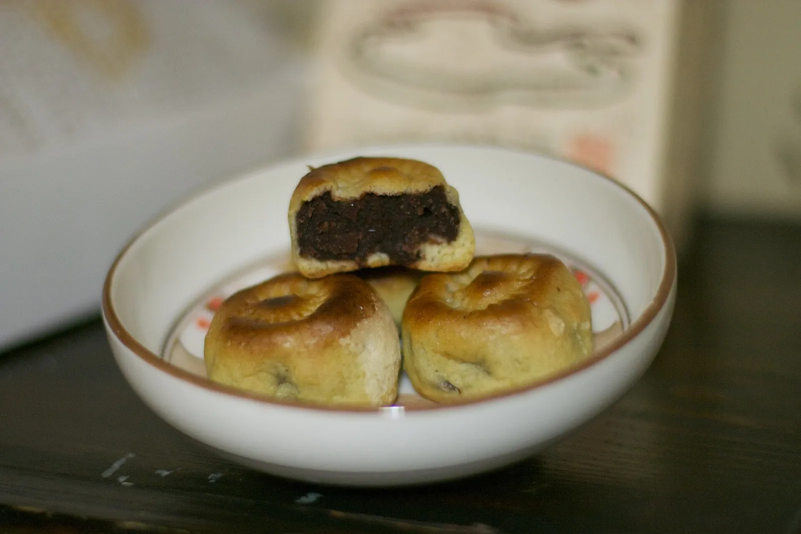 Three Hwangnam-ppang pastries in a white bowl, one broken open to show the red bean filling