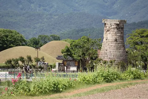 Cheomseongdae stone observatory with grass-covered Silla tombs and hills behind it, Gyeongju