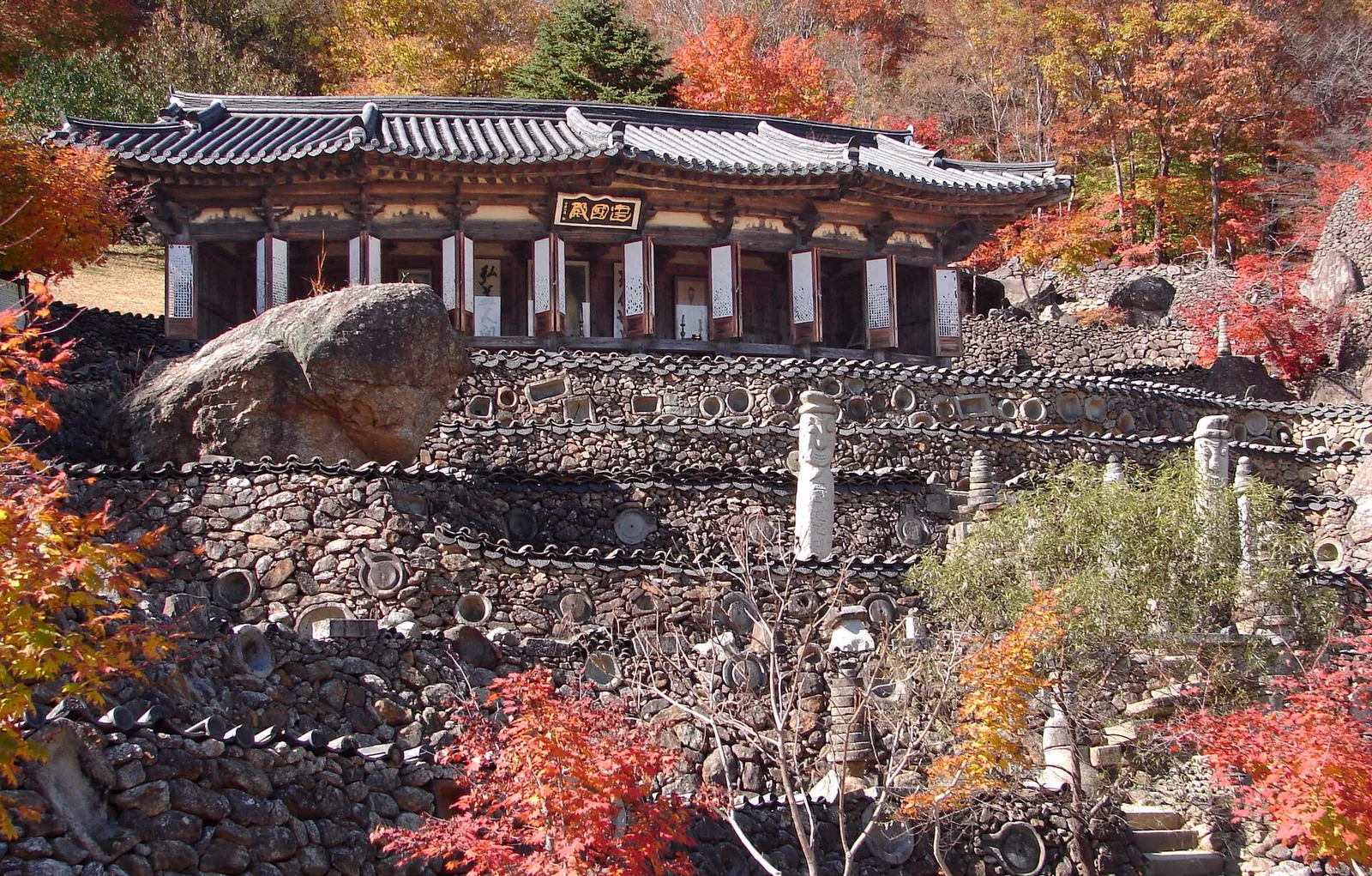 Stone walls and towers below a traditional shrine hall surrounded by autumn maples at Samseonggung