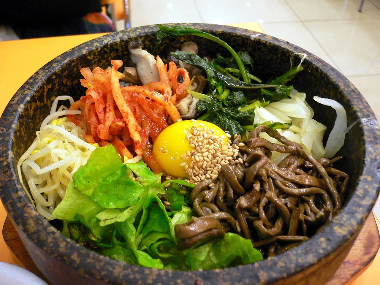 Dolsot bibimbap topped with seasoned vegetables, bean sprouts, greens and an egg yolk