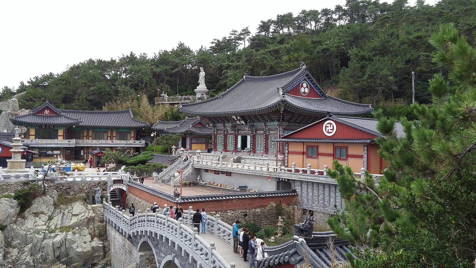 Haedong Yonggungsa temple halls among pine trees above a rocky shore, with a stone bridge in the foreground