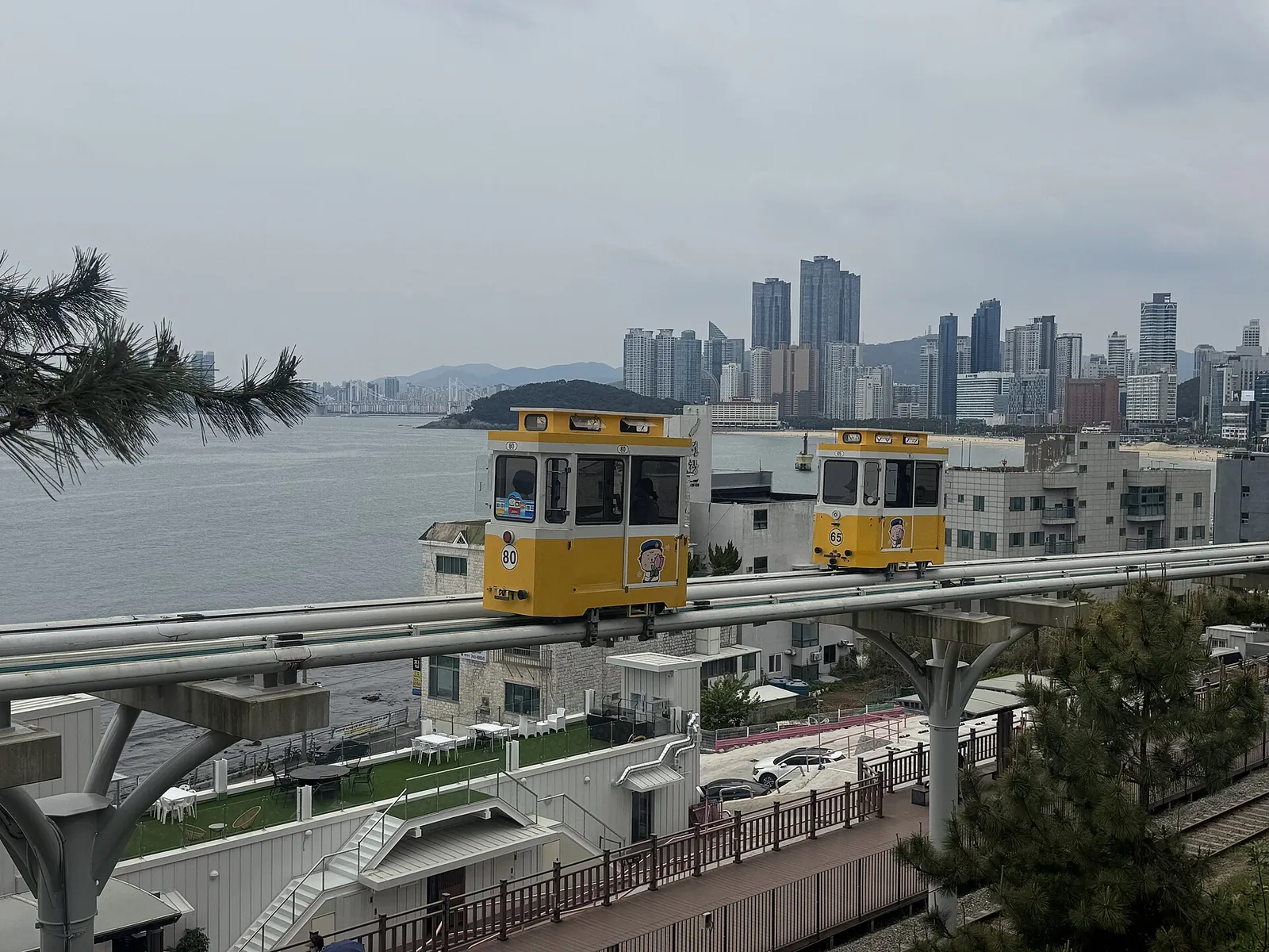 Yellow Sky Capsule pods on the elevated track of Haeundae Blueline Park with the Haeundae skyline behind