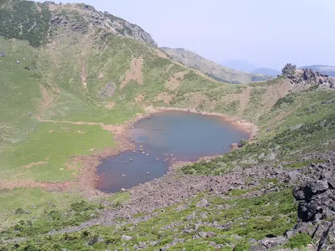 Baengnokdam, um pequeno lago de cratera com margens avermelhadas, na cratera relvada do cume do Hallasan, sob um céu azul pálido