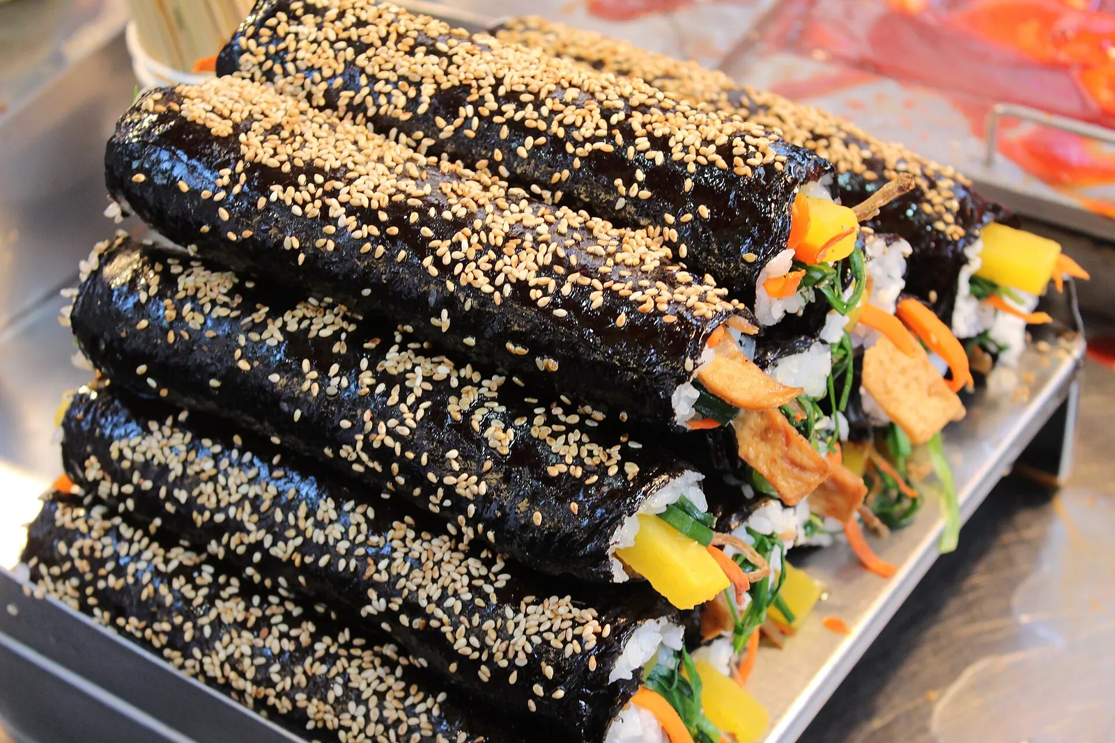 A tray of gimbap rolls sprinkled with sesame seeds, showing rice, vegetables and fillings