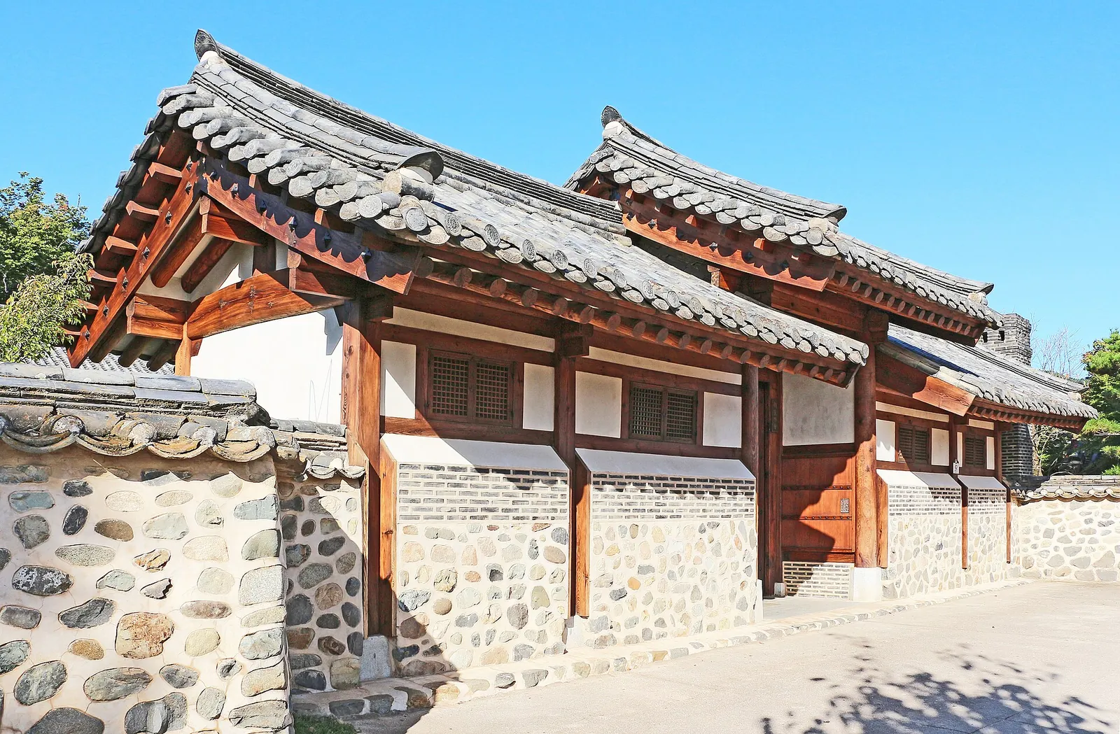 Tiled-roof hanok with timber frame and stone-and-plaster walls under a blue sky in Hahoe Village, Andong