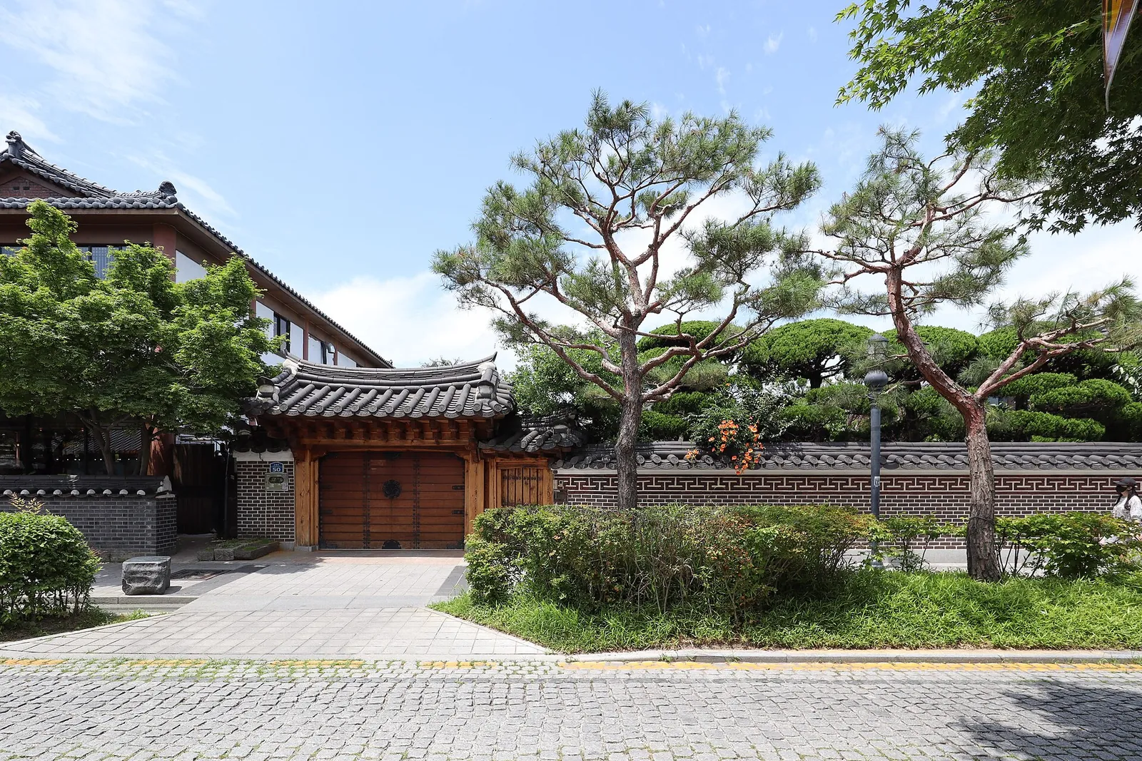 Hanok with a tiled gate, pine trees and a stone-paved lane in Jeonju Hanok Village