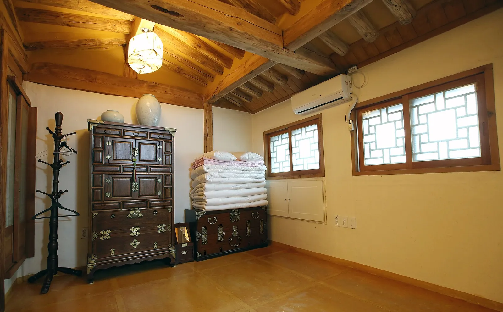 Guest room in a Bukchon hanok stay with a wooden ceiling, lattice windows, a wooden chest and folded bedding stacked against the wall