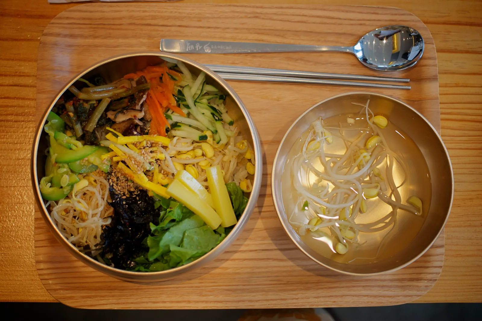 Jeonju bibimbap of rice topped with vegetables in a metal bowl, served on a tray with a bowl of bean sprout soup