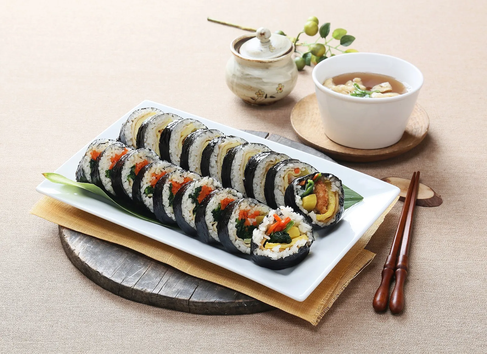 Sliced gimbap rolls on a white plate with a small bowl of soup and chopsticks