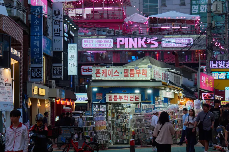 Neon signs, a phone-case stall and shoppers on a busy lane in Hongdae, Seoul