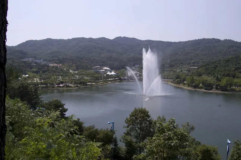 Fountain jetting over the lake in Seolbong Park, Icheon, with wooded hills behind