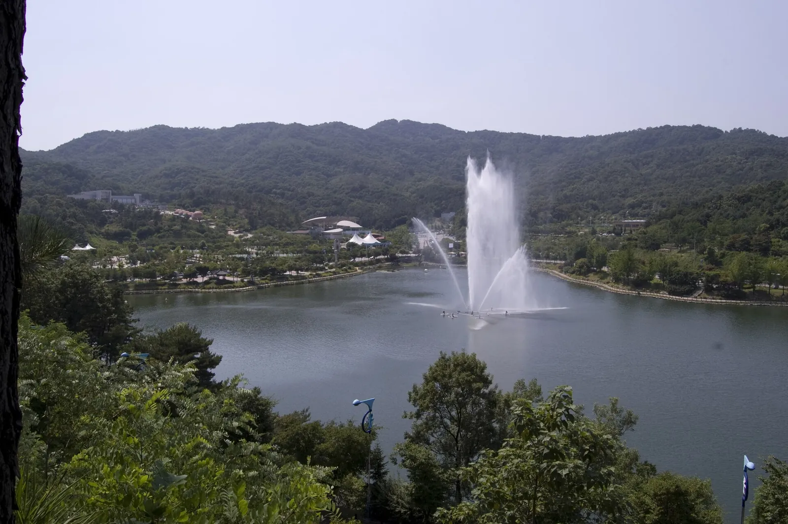 Fountain jetting over the lake in Seolbong Park, Icheon, with wooded hills behind