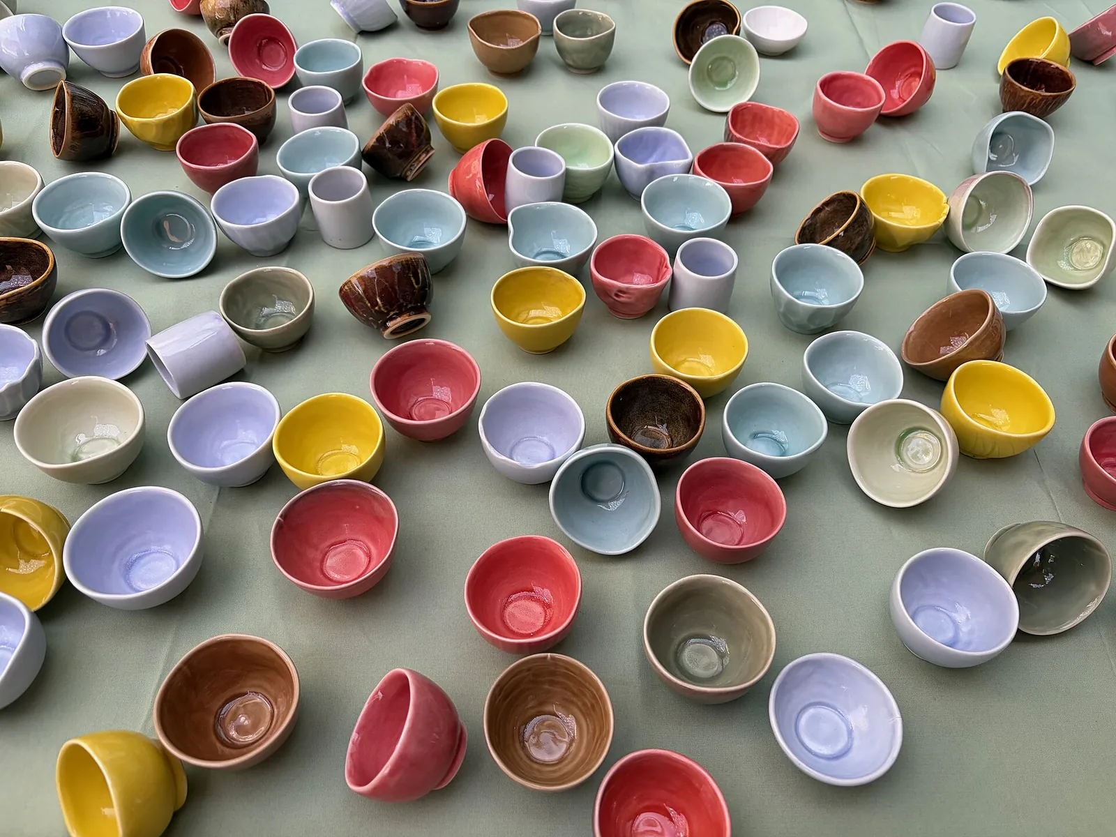 Dozens of glazed ceramic bowls in red, yellow, blue, white and brown spread across a green surface at the Icheon Ceramics Festival