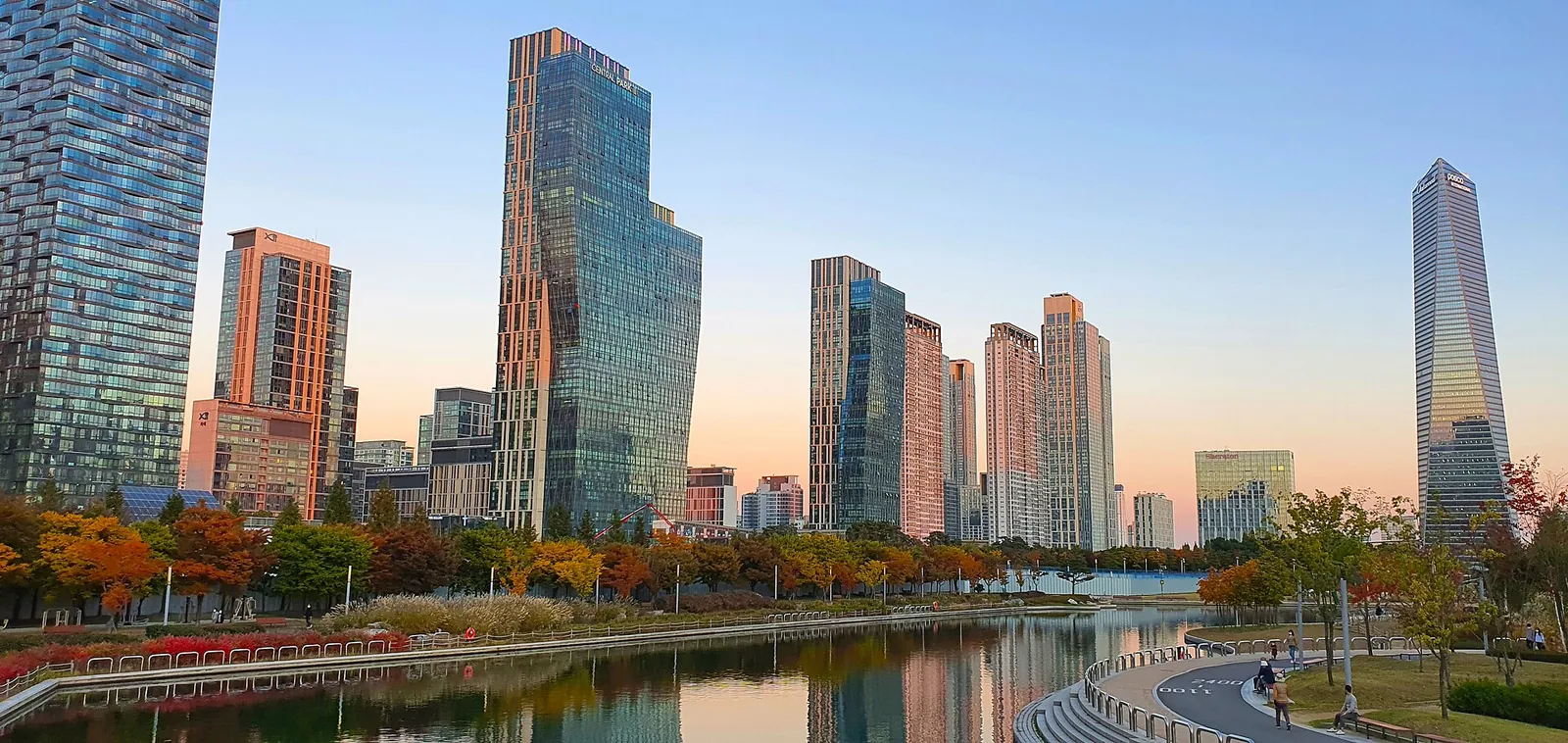 Glass towers of Songdo reflected in the seawater channel of Songdo Central Park, with autumn trees along the bank