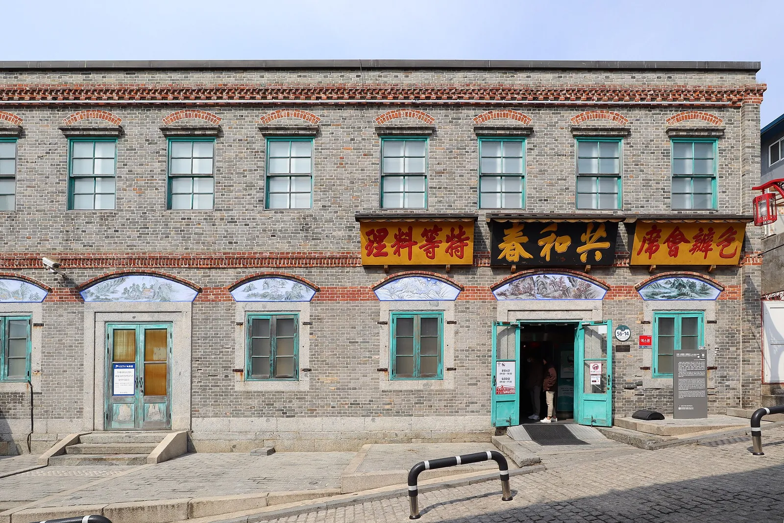 Grey brick two-storey building with green shutters and red Chinese signboards, the former Gonghwachun restaurant