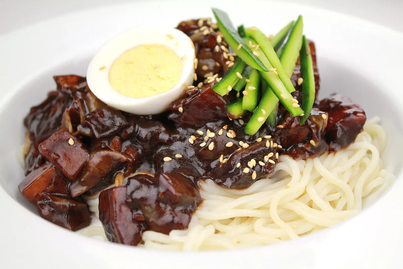 A bowl of jjajangmyeon with thick black-bean sauce over noodles, topped with cucumber strips and half a boiled egg