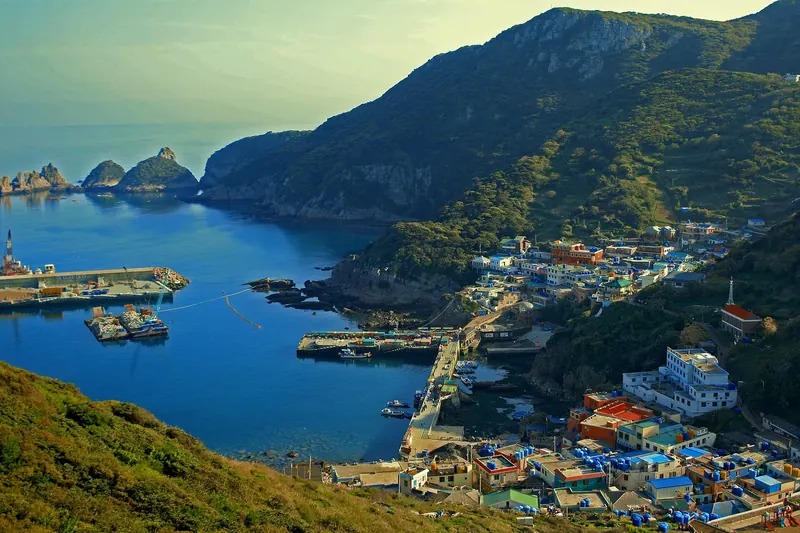 Hongdo Island harbour and village below green cliffs, with rock islets offshore