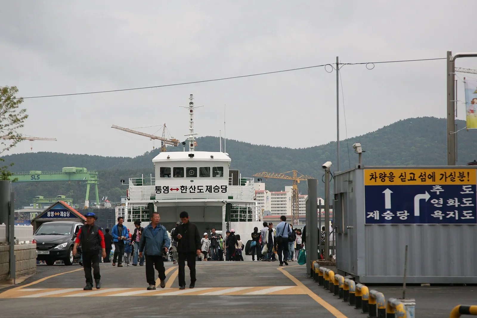Passengers walking from a ferry along the quay in Tongyeong, with island-route signs in Korean