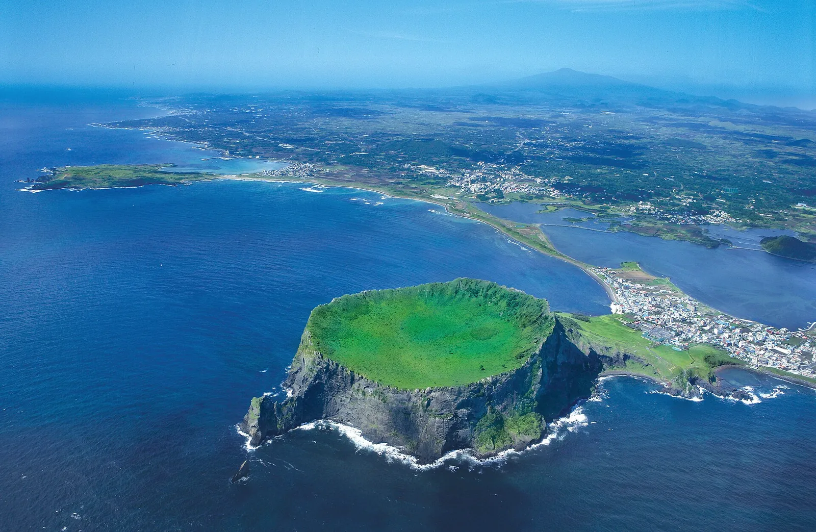 Aerial view of Seongsan Ilchulbong tuff cone with its green crater rim, the village of Seongsan and Jeju's east coast behind
