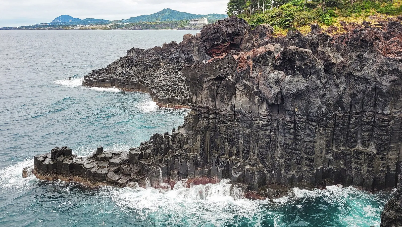 Hexagonal basalt columns of Daepo Jusangjeolli Cliff with waves breaking at their base