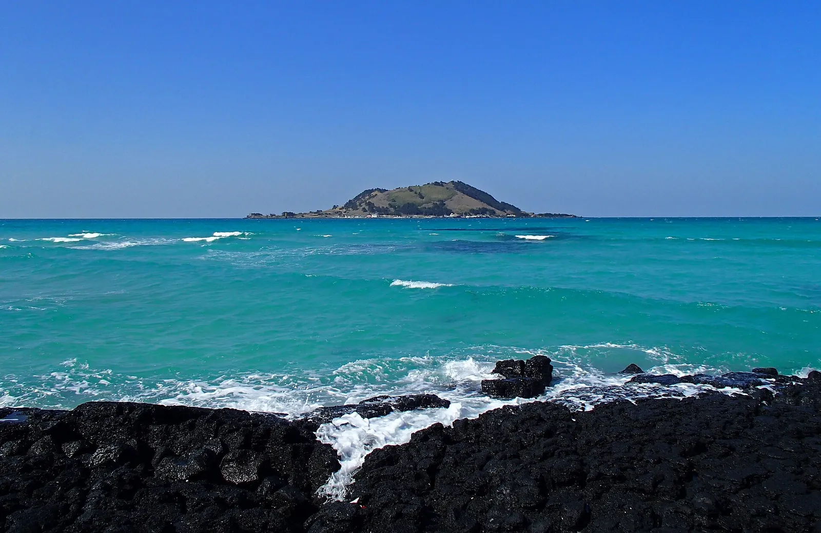 Black volcanic rocks and turquoise sea with the small island of Biyangdo on the horizon, seen from Hyeopjae Beach