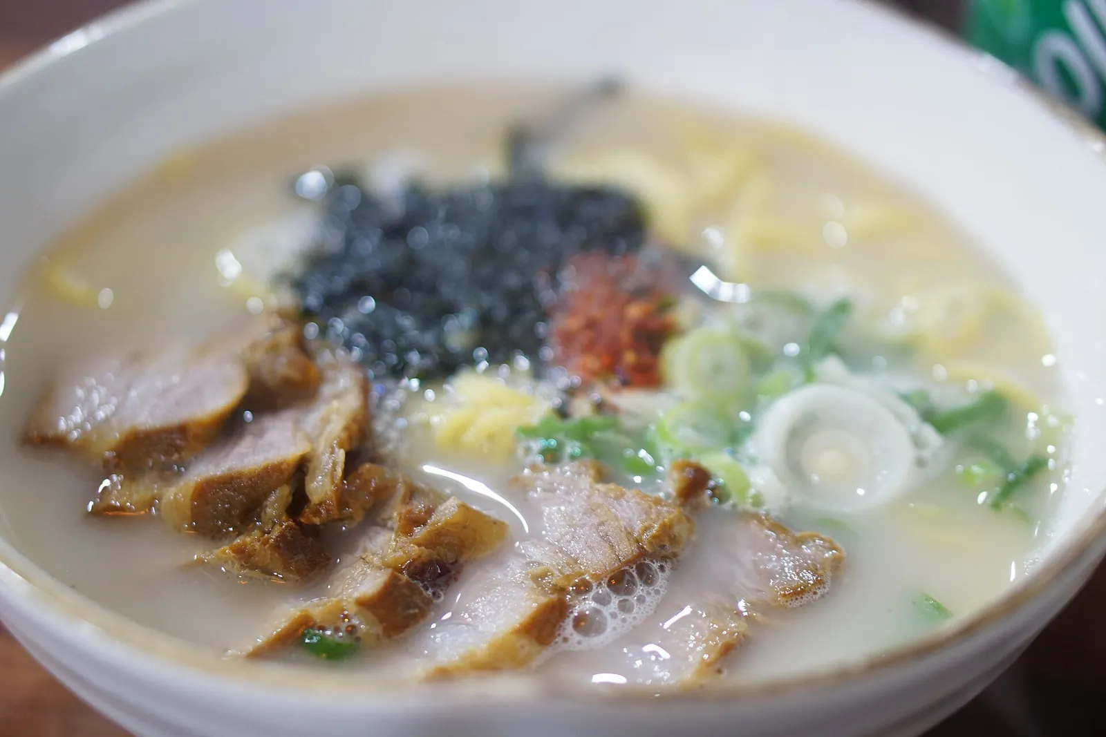 A bowl of gogi-guksu, noodles in milky pork broth topped with sliced pork, seaweed flakes and spring onion