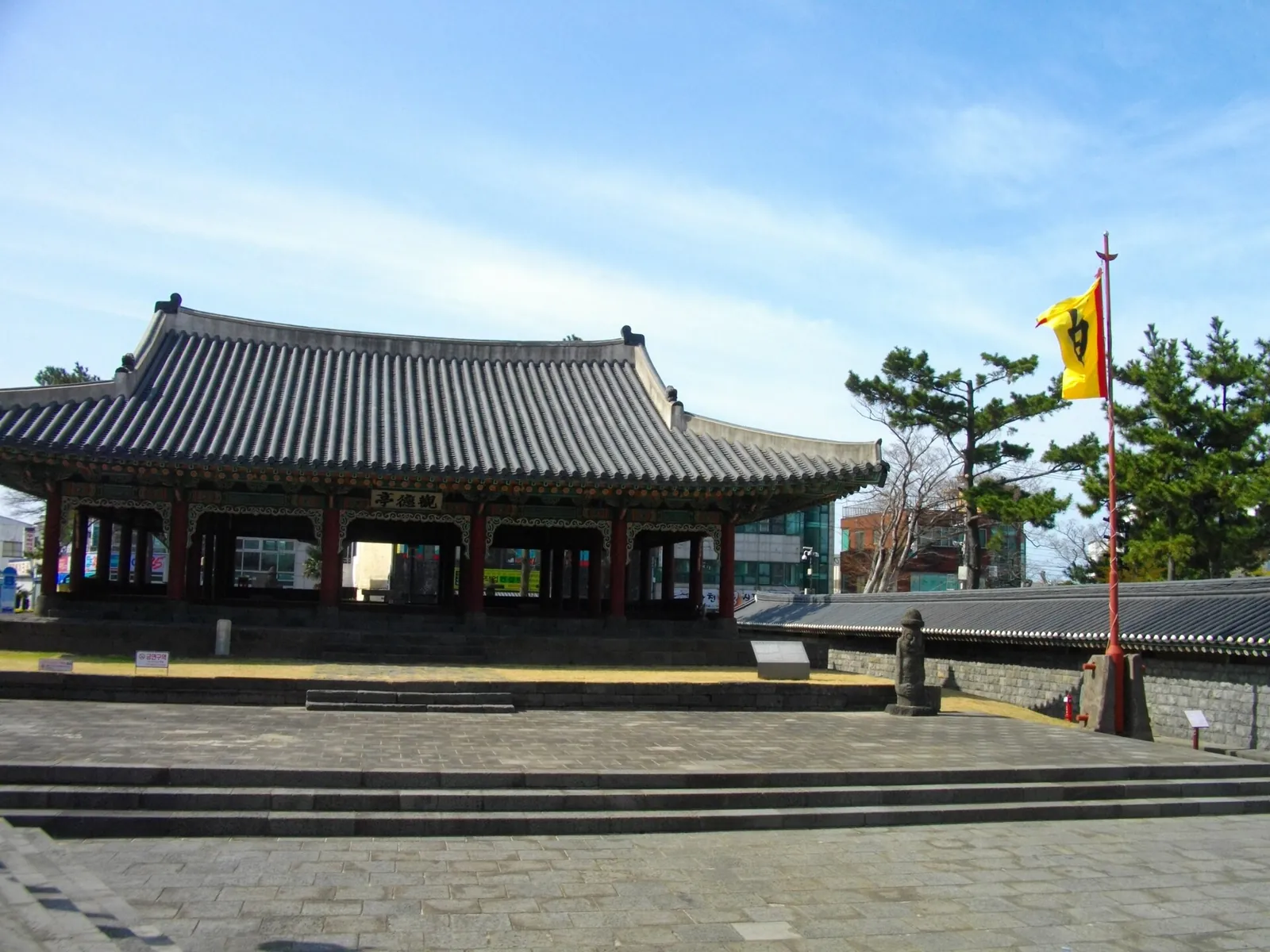 Gwandeokjeong, a single-storey Joseon pavilion with a tiled hipped roof and painted columns, on a stone-paved square under blue sky