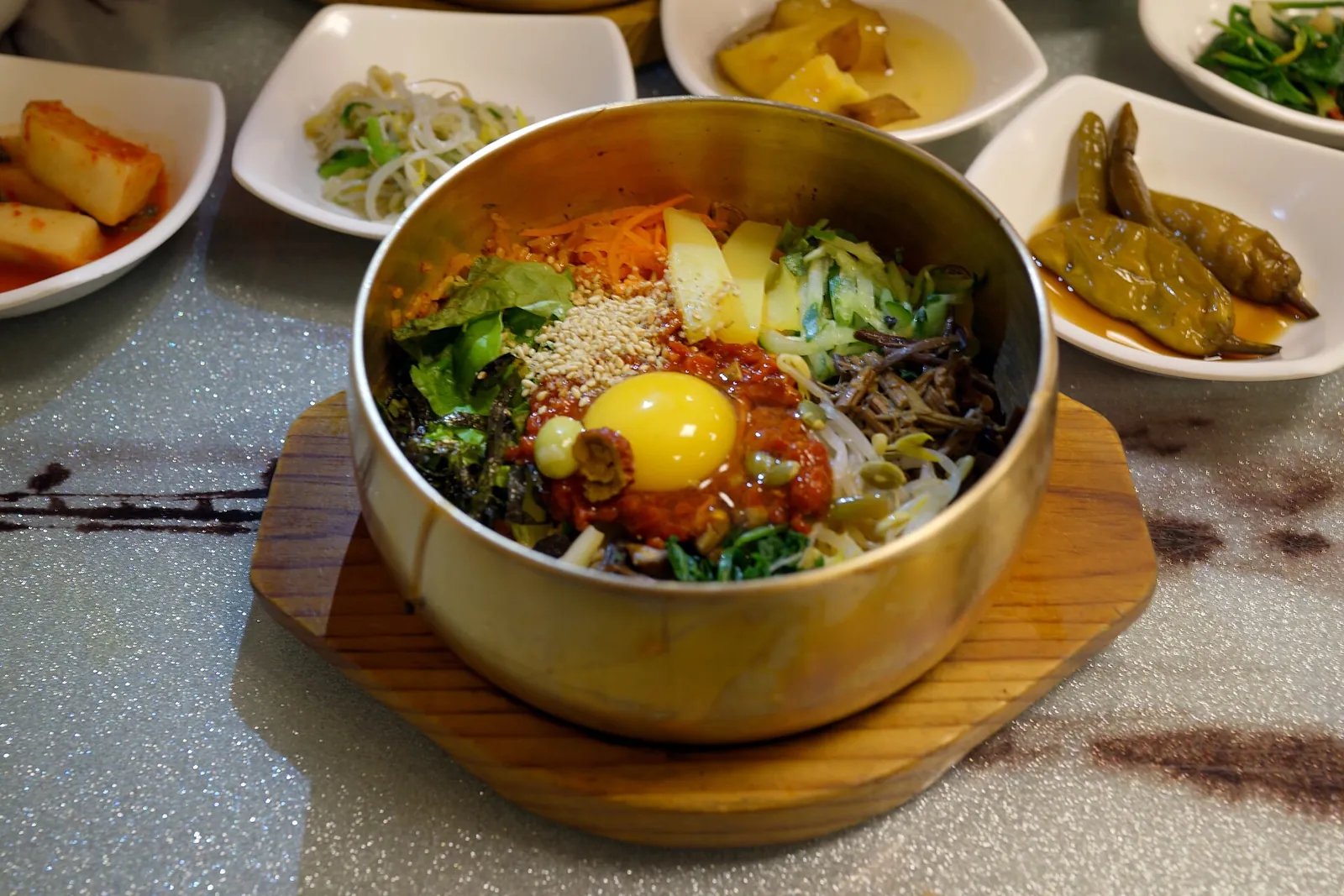 Jeonju bibimbap in a brass bowl topped with an egg yolk, with small side dishes around it